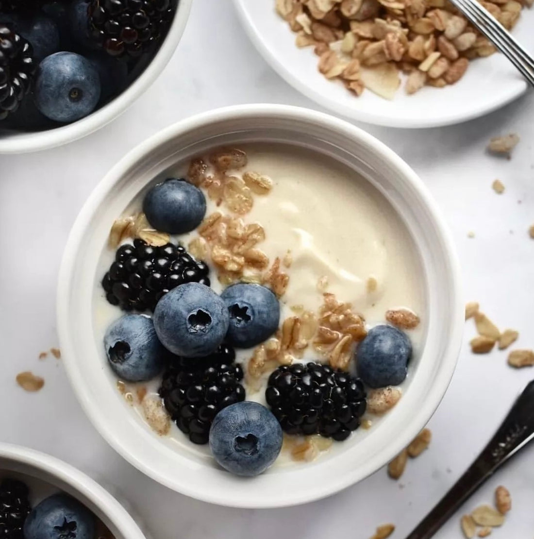 Bicchiere con budino alla vaniglia, lamponi e granola Clemi's Market con due cucchiaini argento e un panno da cucina